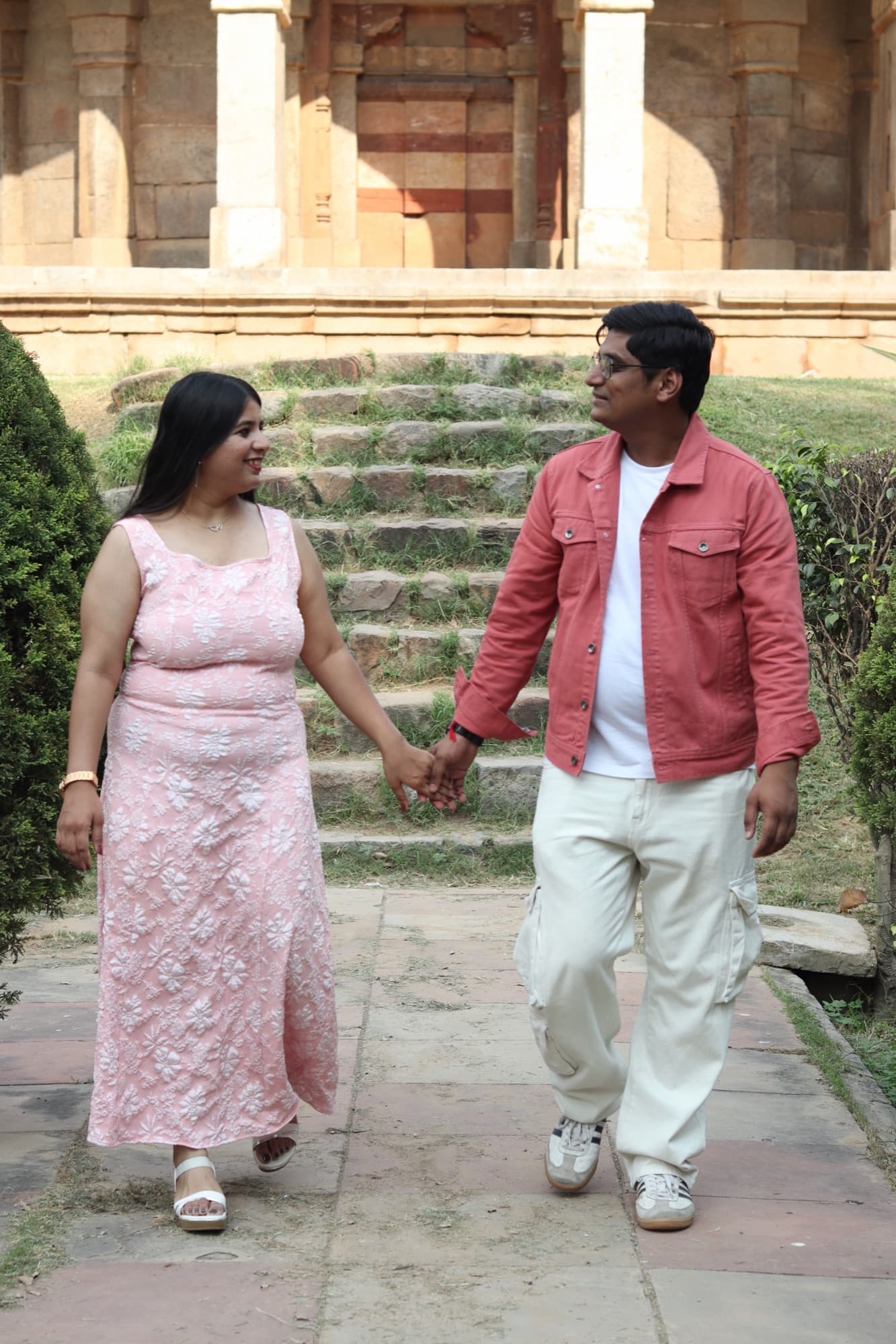 Shubhika and Prayas walking hand in hand in front of a sandstone monument